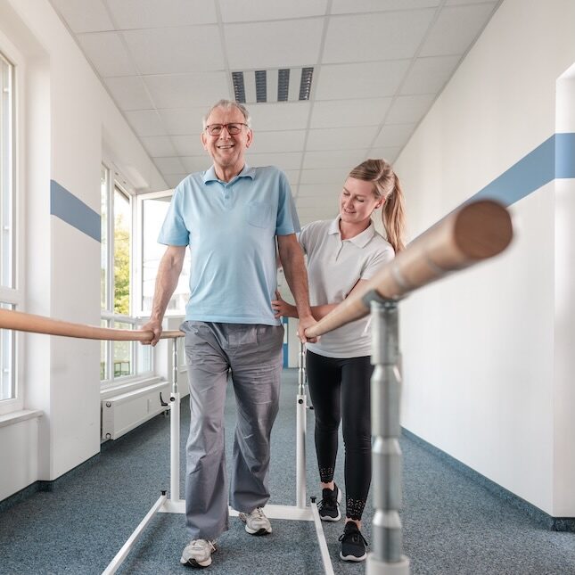 post-op-physio-rails.jpeg Female physio helping a post op physiotherapy patient walk with rails
